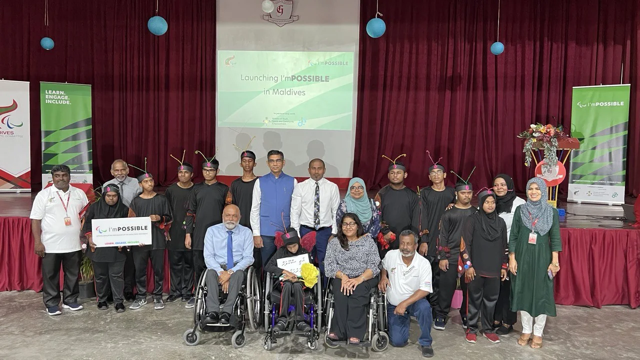 Opening-ceremony guests, young performers and wheelchair users pose together beneath the I’mPOSSIBLE launch screen.