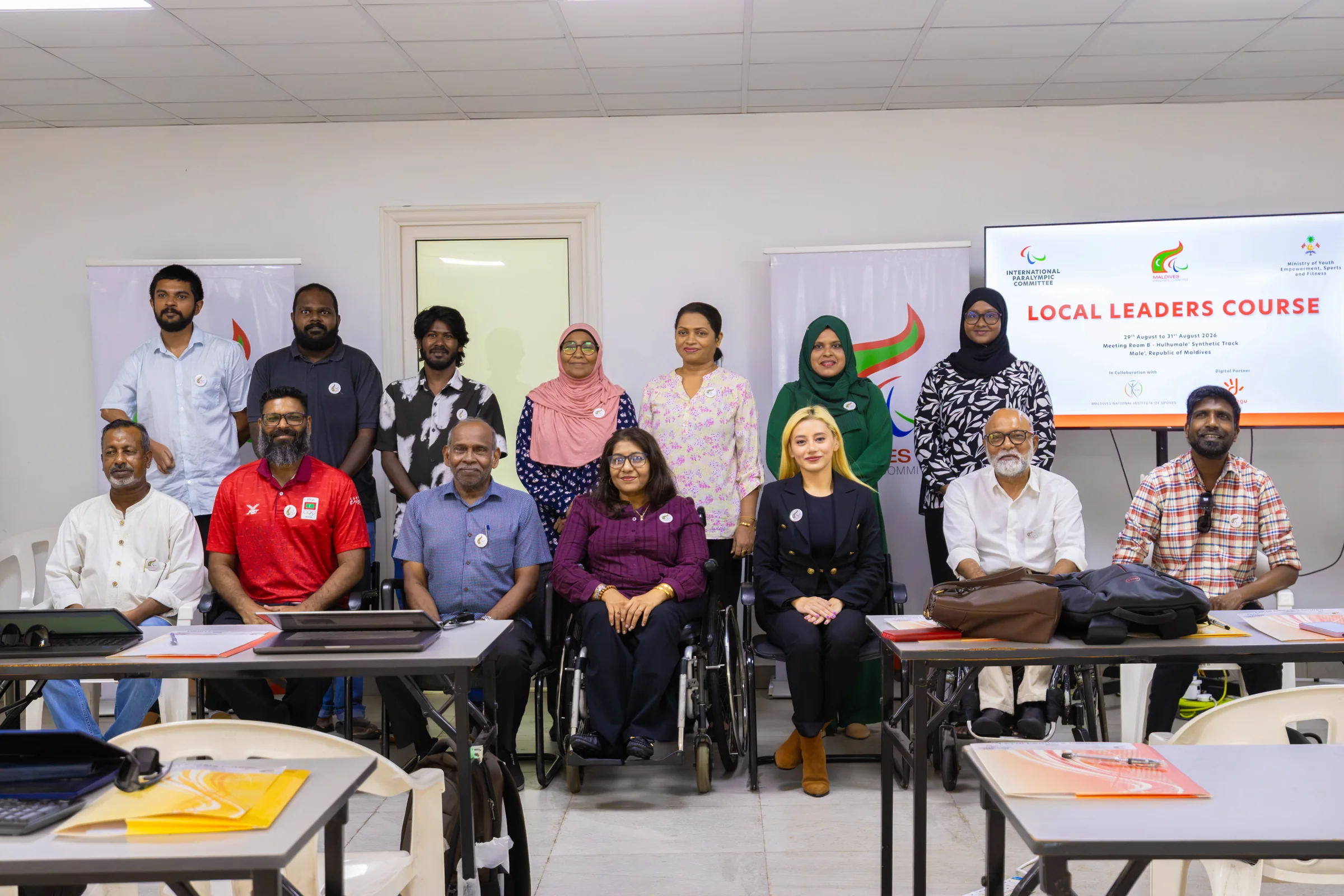A large group poses together in the classroom beneath the Local Leaders Course display.